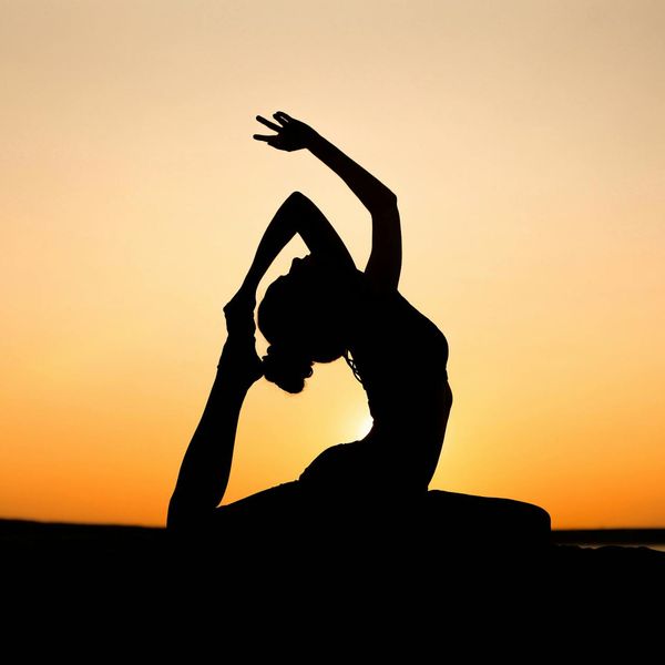 A silhouette of a person in a strong yoga warrior pose against a sunset.